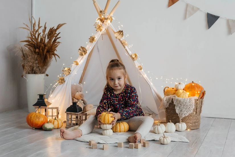 Devojčica okružena jesenjim dekorativnim predmetima, bundeve, lampioni, lišće.
