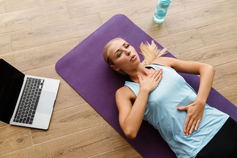 Devojka radi vežbe disanja ležeći na prostirci za jogu.